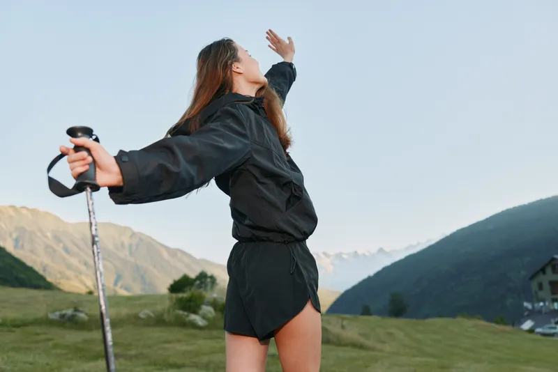 A fit hiker stands outdoors in a scenic mountain landscape, gripping a trekking pole and gazing upward with a sense of freedom and adventure, inspiring motivation and optimism.