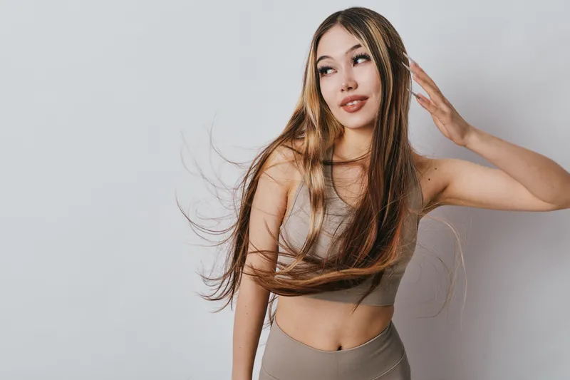 Young woman with long flowing hair looking away posing in beige crop top and skirt on light background studio. Beauty, fashion, hairstyle and modern casual outfit style.