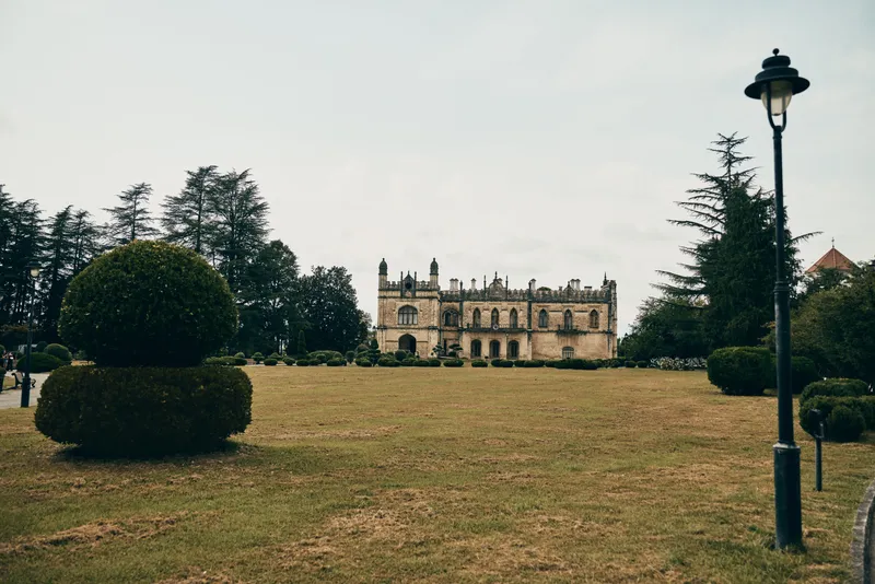 Castle in a manicured park with trimmed hedges and a vintage lamppost, showcasing historic architecture and expansive green grounds in a serene outdoor setting.