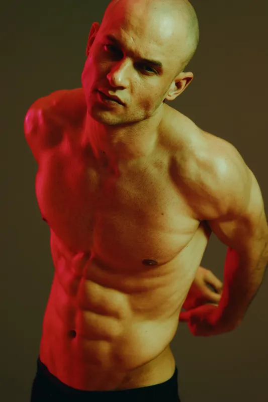 Confident man posing, showcasing toned physique and strong expression, with a focus on body language and lighting, creating a compelling visual impact.