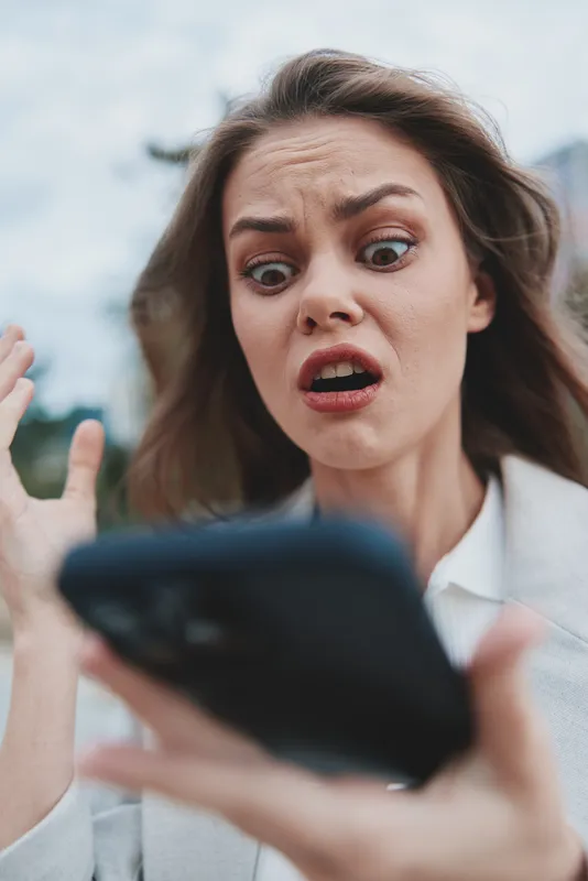 Woman shocked by financial crisis looking at phone with worried expression outdoors business concept emotion KEY: financial crisis, woman, phone, shocked, worried, business, emotion, stress, outdoors,