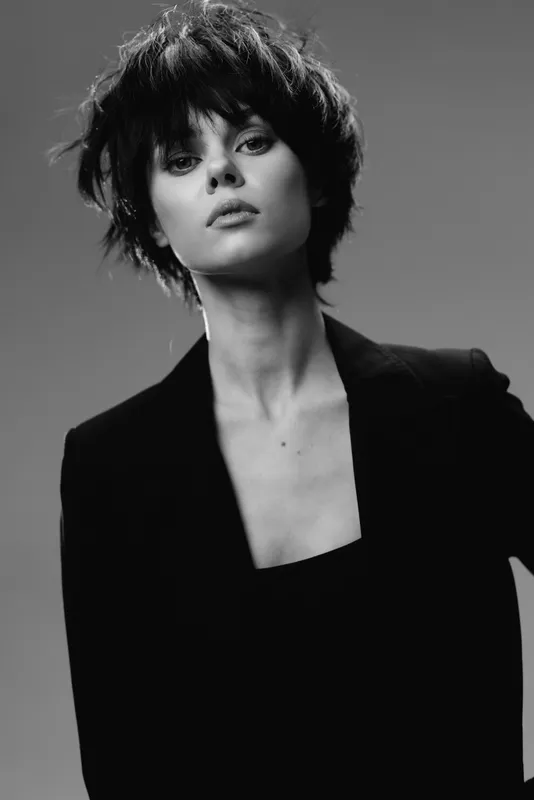 Black and white portrait of young woman with short hair wearing a blazer, expressing confidence and style in studio lighting.