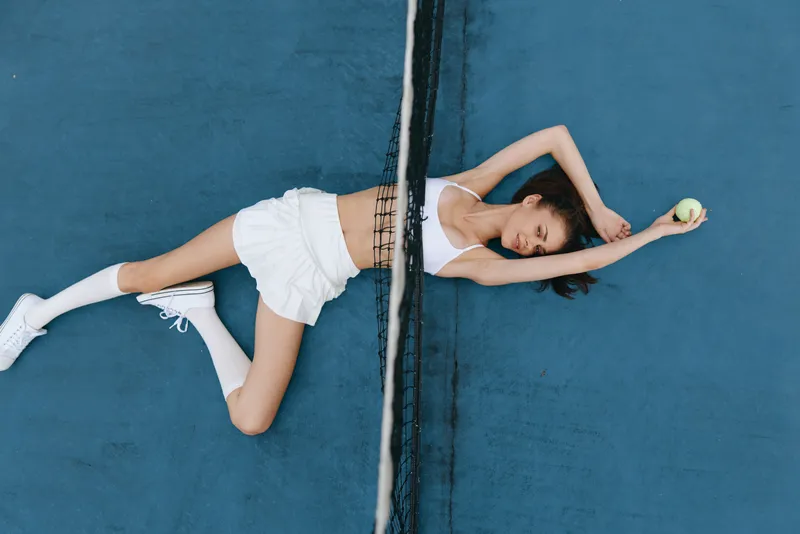 Athletic young woman in sporty attire relaxing on a blue tennis court, demonstrating confidence and serenity with a tennis ball in hand