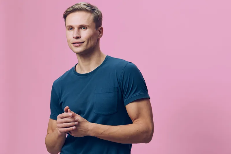 Confident man with short hair wearing navy blue t-shirt stands against pink background. Studio portrait with casual relaxed pose, natural expression, modern style. People lifestyle concept.