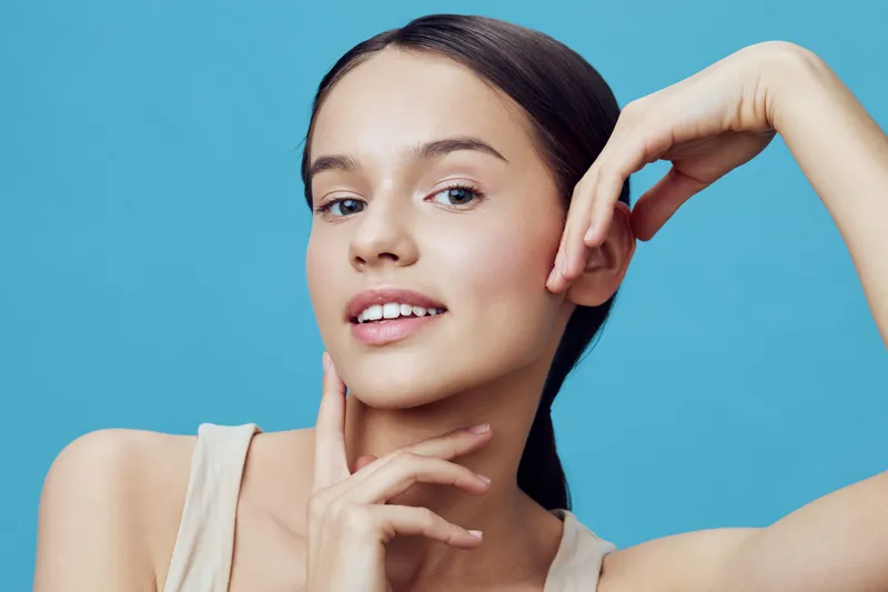Portrait of a young smiling woman with smooth skin on a blue background, showcasing beauty and confidence, wearing a light top, perfect for skincare and beauty concepts