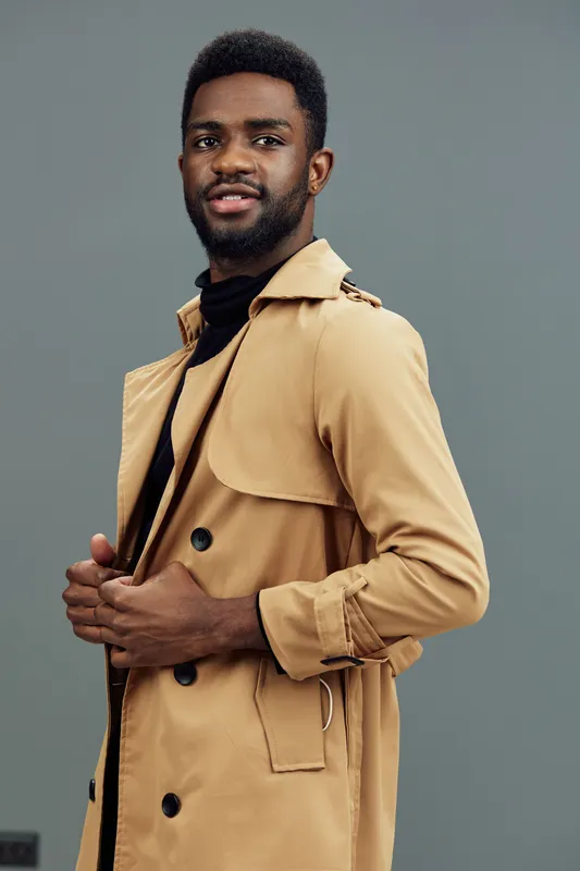 Stylish young man in a beige trench coat against a gray background, showcasing confidence and modern fashion aesthetics for seasonal campaigns