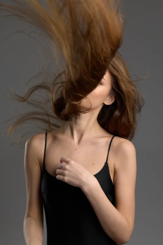 Woman with flowing hair in black dress posing with gray background and dynamic movement.