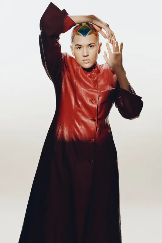 avant-garde woman with colorful geometric hairstyle wearing a red high-fashion coat, striking pose on minimalist white background, artistic and stylish concept