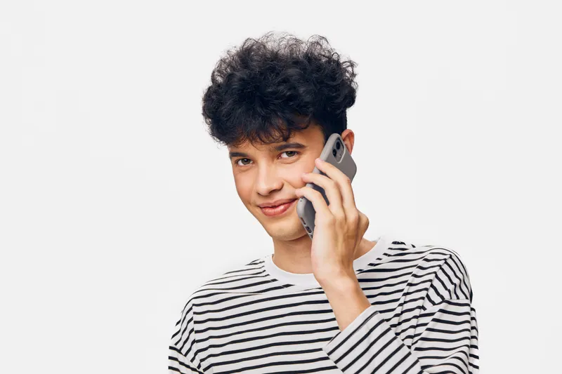 young man talking on smartphone smiling, casual striped shirt, curly hair, light background, communication, modern lifestyle, technology