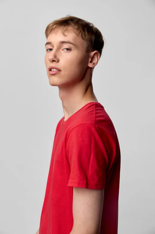Young man in a red shirt, side profile in a studio, casual fashion, clean background, relaxed mood and minimal lighting for modern lifestyle imagery