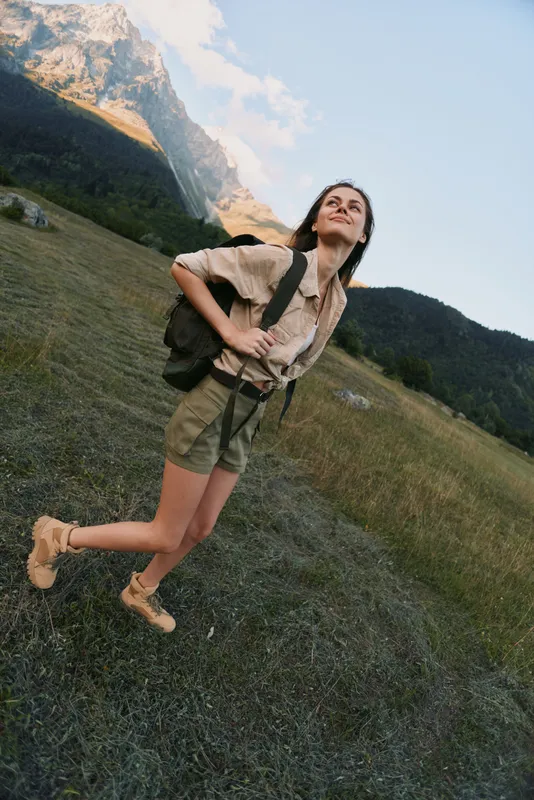 A woman on a sunny hillside enjoys hiking, outdoors, and travel with a backpack, embodying adventure in a vast mountain landscape, clear sky, and peaceful nature.