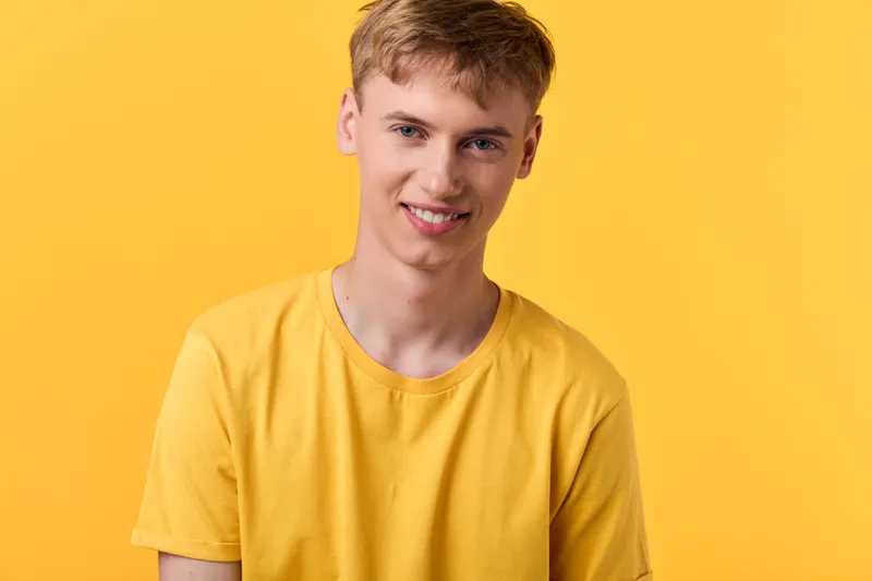 Smiling man in a casual yellow shirt stands against a vibrant yellow backdrop, conveying friendly energy, optimism, and contemporary style for lifestyle stock imagery collection