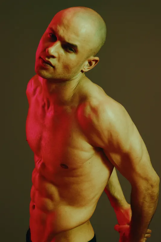 Strong man posing with dramatic lighting, showcasing his physique in a captivating manner. The color contrast emphasizes his muscular form and creates an engaging visual experience.