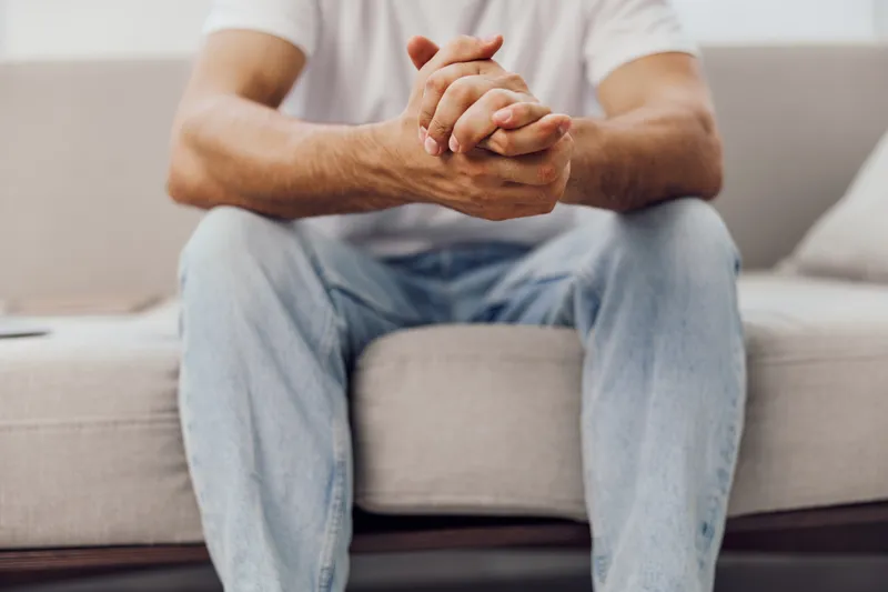 Thoughtful man wearing casual clothes sits on a cozy sofa, reflecting on ideas in a modern interior, evoking a sense of calm and introspection.