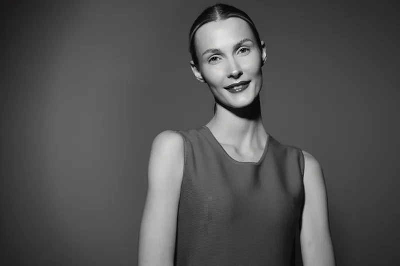 Portrait of a smiling Caucasian woman with light skin and pulled back hair wearing a sleeveless top against a monochrome background. Concept for beauty and confidence.