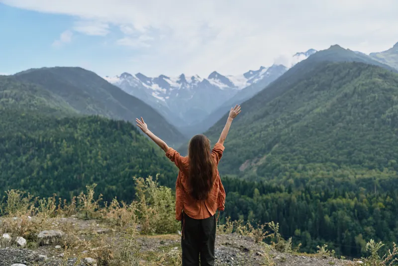 A woman stands with arms raised in a dramatic mountain landscape, embracing the outdoors and capturing a moment of freedom, awe, and vast scenery