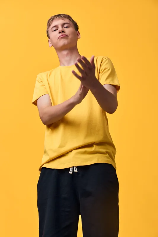 Youth in a bright yellow shirt stands against a vivid background, hands raised in a clap, conveying energy and confidence with casual athletic style suitable for lifestyle and fashion stock