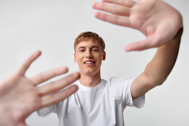 Hands reaching toward the camera with a smiling young man in a white tee creating a friendly connection, dynamic foreground gesture, conveying welcome collaboration help and active engagement in
