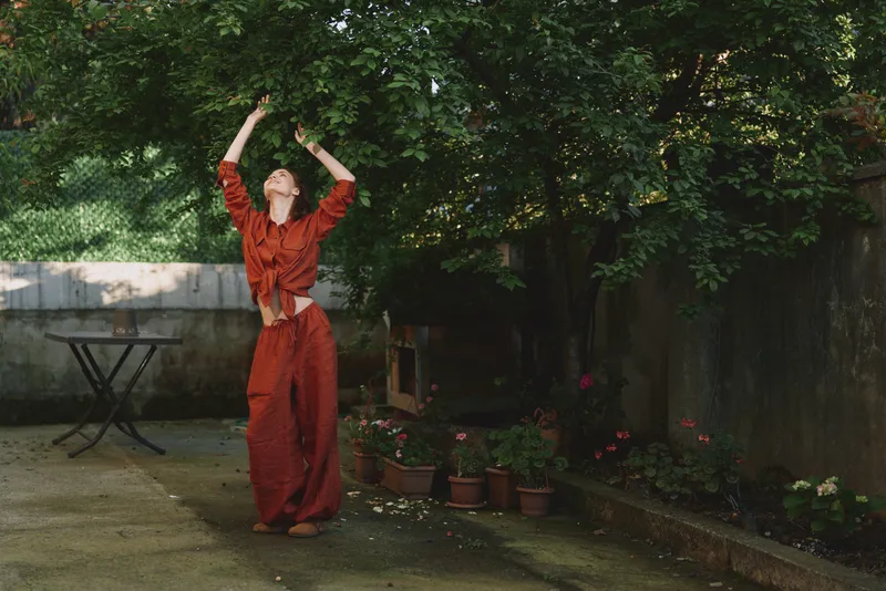 Woman enjoying outdoor lifestyle, dancing in a red outfit in a garden, sunlight through leaves, joyful pose, vibrant colors, natural mood, serene atmosphere