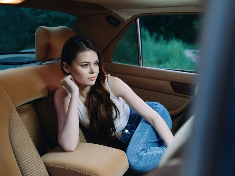 Young woman in casual attire relaxing in a car, expressing thoughtful emotions with a natural outdoor background, capturing the essence of leisure and tranquility.