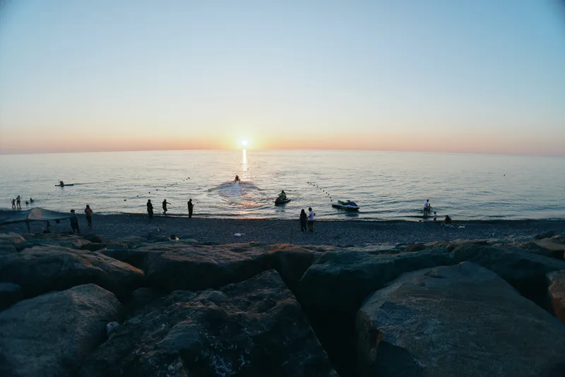 Lifestyle woman in modern boho-western denim street style enjoying sunset on rocky beach with film color tone creating relaxed atmosphere and natural beauty.