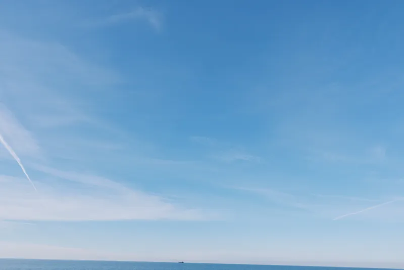 Blue sky over calm sea with distant horizon and wispy clouds, minimal landscape usable as nature backdrop for travel, advertising or editorial projects, conveys serenity and openness