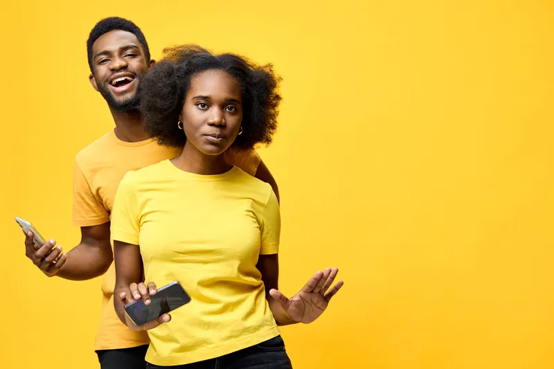 Young African couple wearing yellow shirts, smiling and posing playfully against a bright yellow background, conveying happiness and joy with a vibrant style