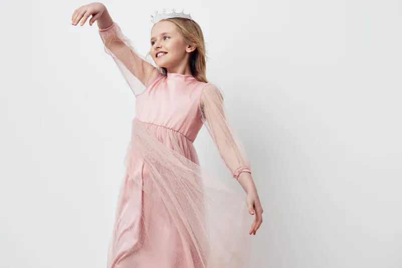Young girl in a pink dress dancing joyfully, showcasing elegance and grace, with a delicate crown against a clean white background, symbolizing childhood happiness