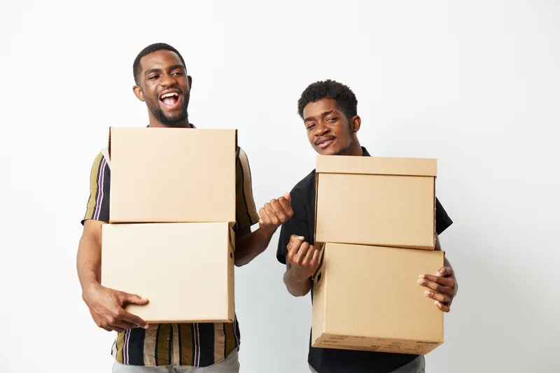 Two African American men joyfully holding cardboard boxes, embracing teamwork and collaboration. Bright, positive atmosphere signifies excitement and readiness for action.