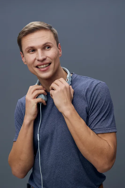 smiling young caucasian man holding headphones looking aside wearing blue casual t-shirt isolated on gray background digital detox mental health concept