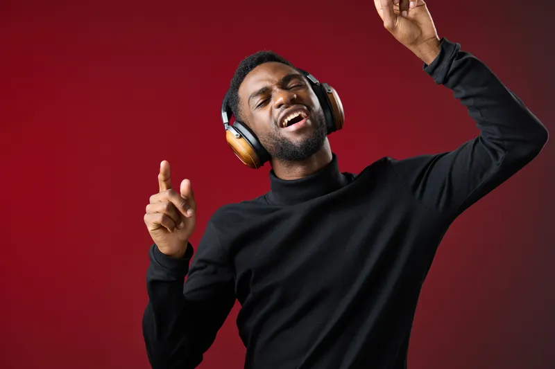 Young Black man enjoying music with headphones, dancing joyfully against a vibrant red background, conveying happiness and passion for music