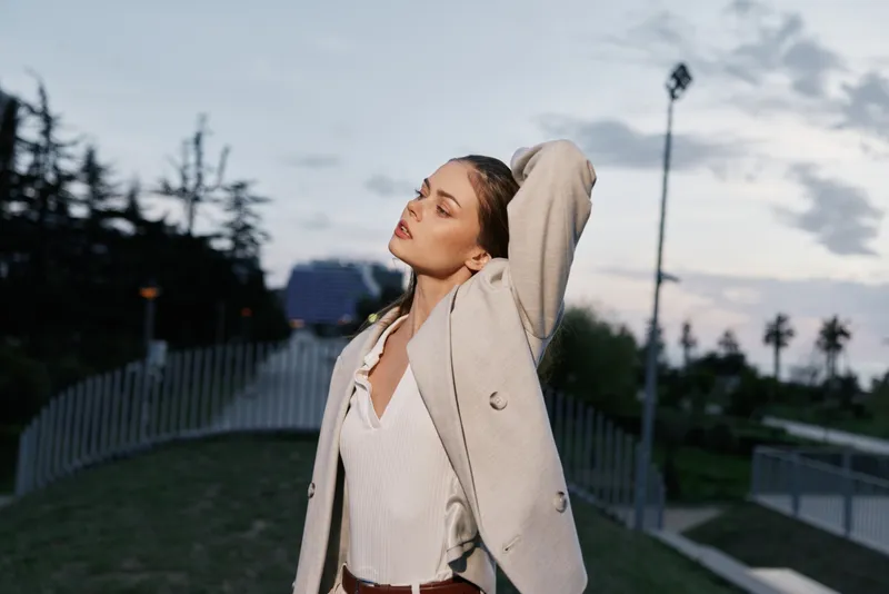 Confident woman in a business suit poses against an evening sky, showcasing professionalism and elegance in an urban setting.