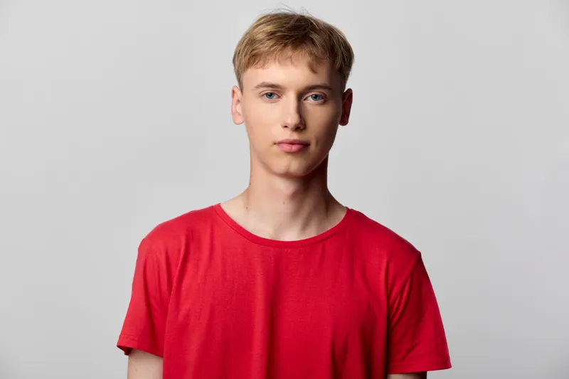 Male model wearing a red t shirt stands against a neutral studio background, presenting a clean casual look suitable for fashion and lifestyle imagery, highlighting approachable style and
