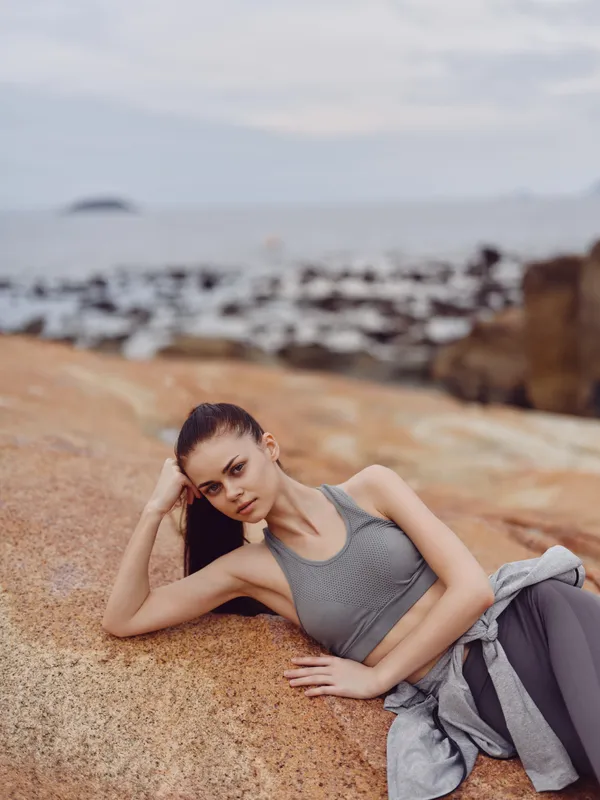 Fitness model in activewear resting on rocky beach, showcasing strength and calmness Healthy lifestyle concept with ocean background and natural colors