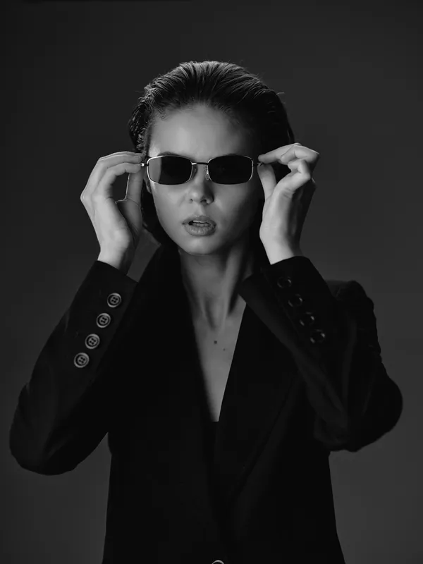 black and white woman wearing sunglasses and a blazer with serious expression in studio