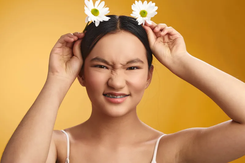 asian woman with daisies on her head, playful expression, bright yellow backdrop, creating a joyful, vibrant mood ideal for lifestyle and fashion stock use.