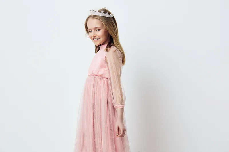 A joyful young girl wearing a pink tulle dress and a crown, showcasing happiness and innocence against a minimalist white background