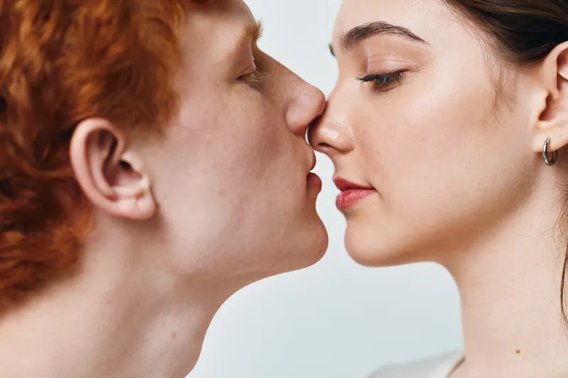 Couple closeup, romantic moment with man and woman touching noses, intimacy and love expression with closed eyes on light background studio portrait.