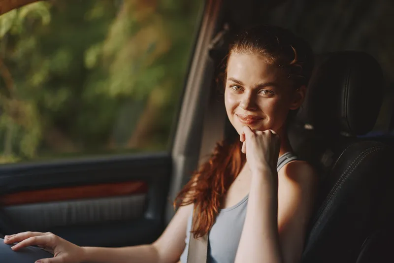 Young woman smiling in a car, wearing casual athletic clothing, with a nature background, showcasing joy, confidence, and a serene summer atmosphere