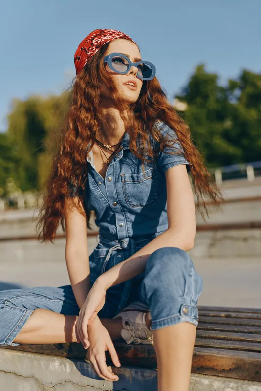 lifestyle woman in modern boho-western denim street style wearing blue sunglasses and red bandana with film color effect under natural sunlight outdoors