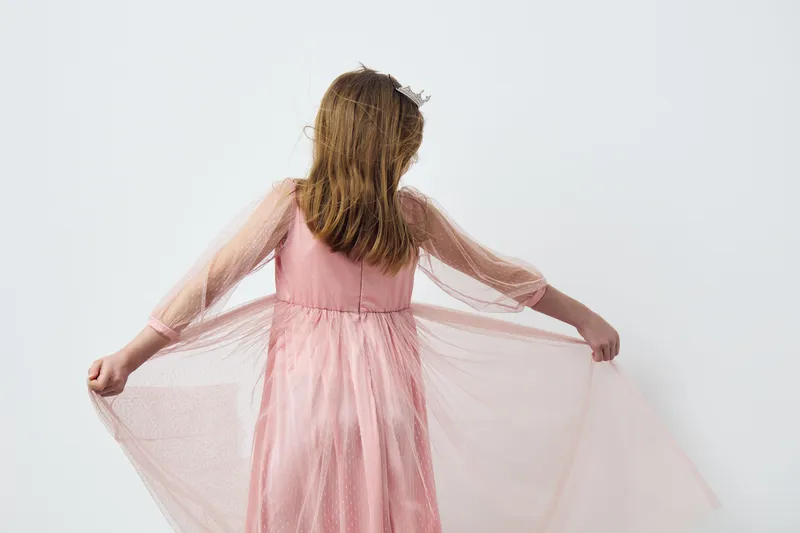 Young girl in a flowing pink dress, joyfully dancing, showcasing innocence and beauty against a minimalist white background, perfect for children s fashion themes