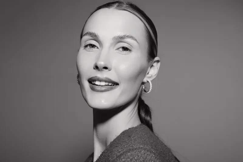 Portrait of a smiling Caucasian woman with light skin and pulled back hair wearing earrings and a sweater against a plain background. Concept of beauty and confidence.