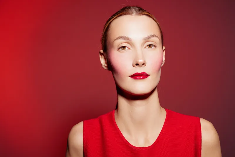 Portrait of a woman with red lipstick and red dress against red background. Minimalist style with soft lighting highlights facial features and smooth skin texture.