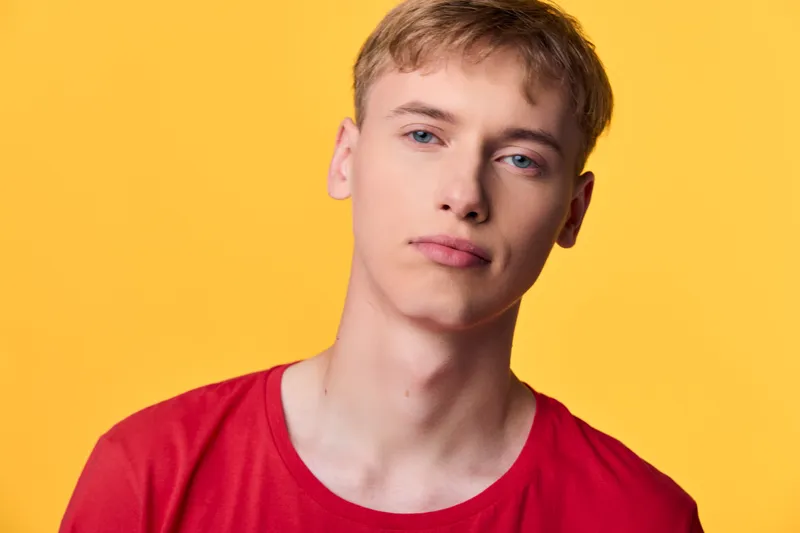 Closeup of a young man in a red shirt against a bright yellow background, showcasing casual fashion, confident pose, and clean studio lighting with sharp detail