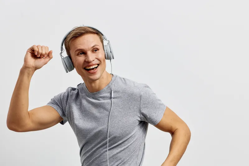 Smiling man listening to music with headphones, enjoying dance and movement, casual grey t-shirt, energetic mood, isolated on plain white background, studio portrait. People lifestyle concept