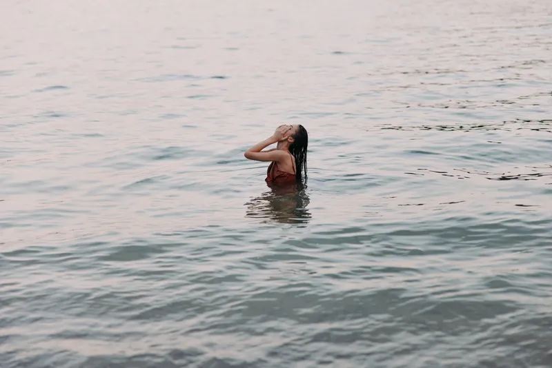Woman swimming alone in calm water, enjoying serene sunset outdoors with peaceful nature, relaxation, and summer vibes.