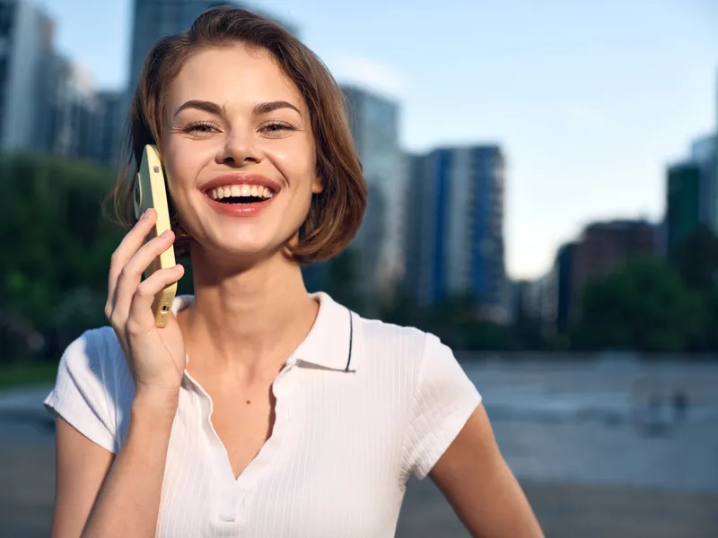 A cheerful business professional is seen texting in a modern outdoor city environment. She smiles and appears engaged, creating a positive and dynamic atmosphere.