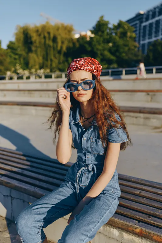 Lifestyle woman in modern boho-western denim street style wearing blue sunglasses and a red bandana, captured in vibrant film color lighting outdoors.