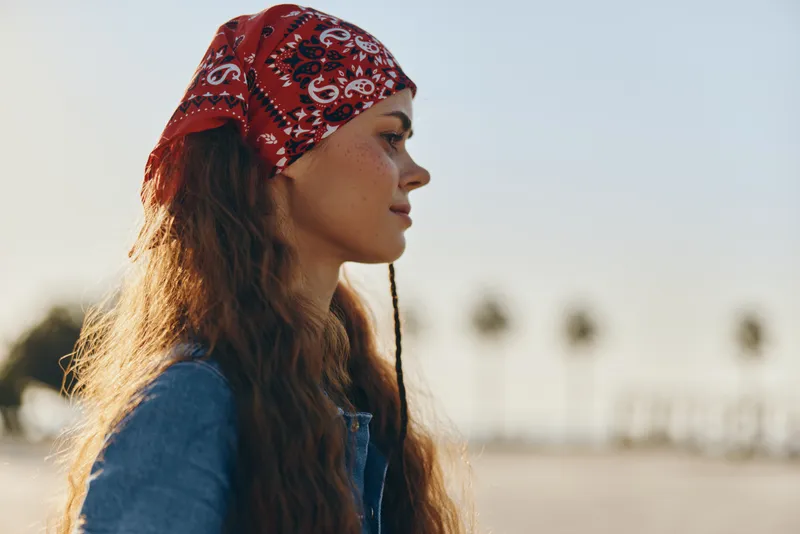 lifestyle woman in modern boho-western denim street style wearing red bandana, long hair, warm light, film color tones, outdoor sunny atmosphere
