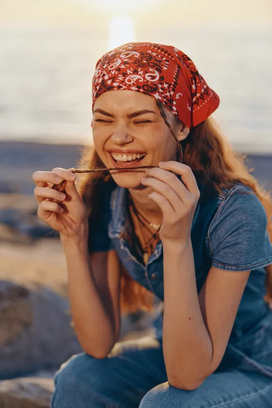 Lifestyle woman wearing modern boho-western denim street style laughing with a red bandana at sunset, enjoying carefree joyful moments in natural film color light.